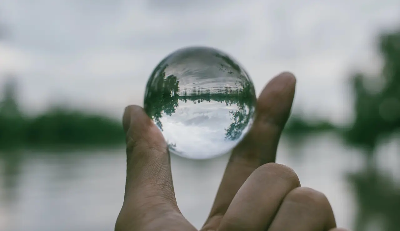 A hand holding a transparent glass sphere while looking out towards the lake